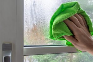 Male hand cleaning condensate on a plasic framed window with a microfiber cloth. Cold season. Temperature difference.