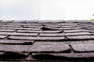 Close-up on damaged asphalt shingles over the roof of a shed in the backyard