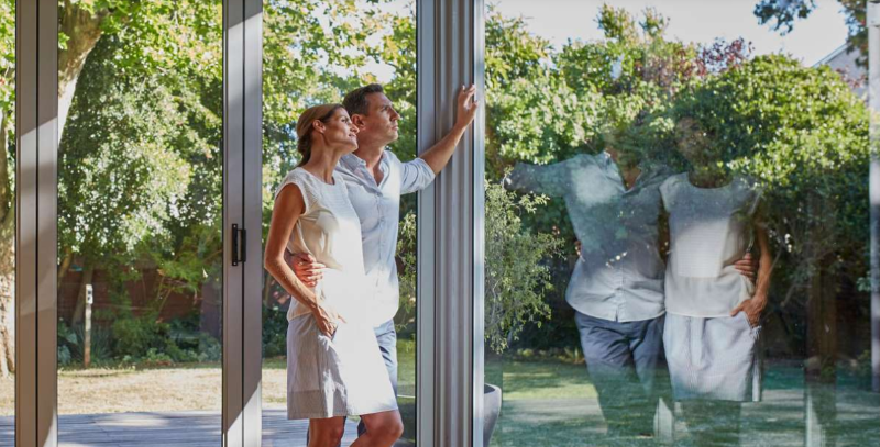A photo of a man and a woman, standing next to a window made of Neat Glass, looking outside.