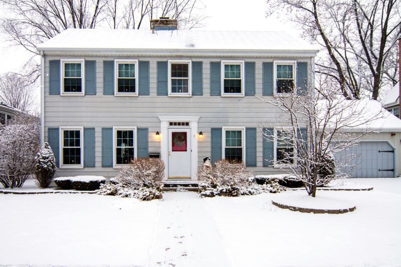 A photo of a two-story home in winter. The house has a white front door and multiple windows on both flooors.