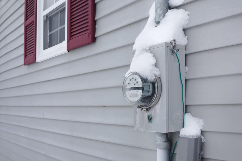 A photo of a power meter on the side of a house, covered in snow.