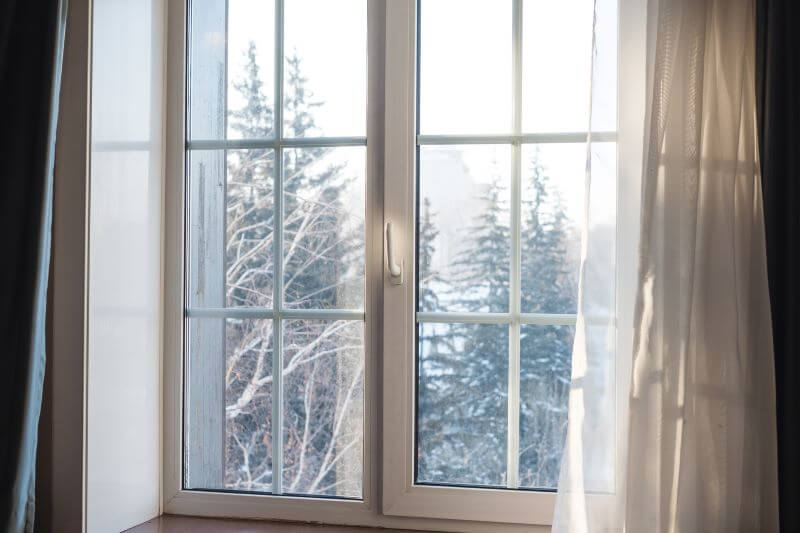 A photo of a window in a house, overlooking trees covered in snow.
