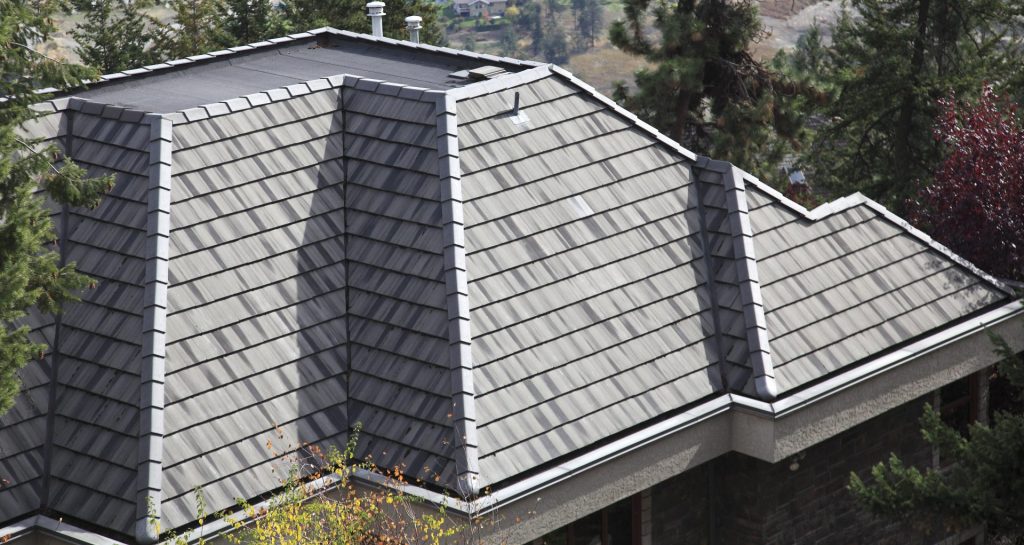 Close-up view of a residential roof featuring gray synthetic shingles with a clean, geometric layout surrounded by trees.