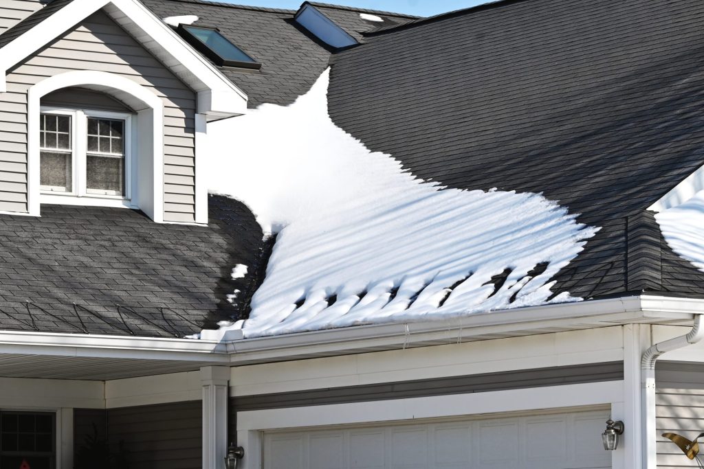 House roof with snow melting over dark impact resistant shingles, featuring skylights and a heat cable system in winter.