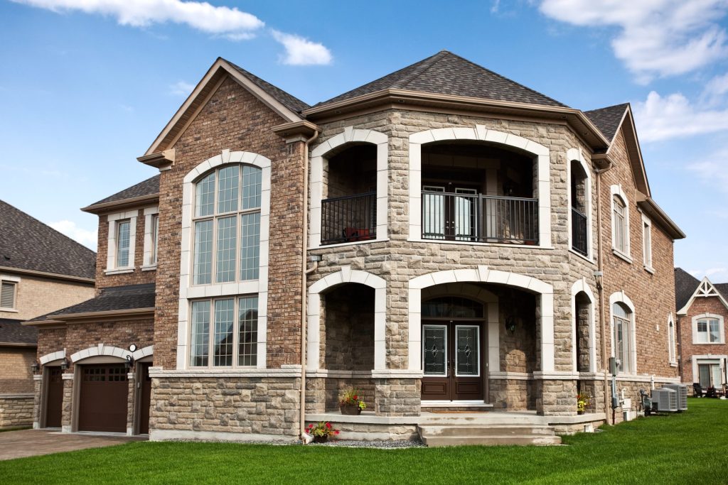 Large two-story stone and brick home with dark roofing, showcasing durable roofing materials and a grand front entry.
